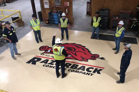 razorback concrete team gathered around for safety meeting, logo on floor